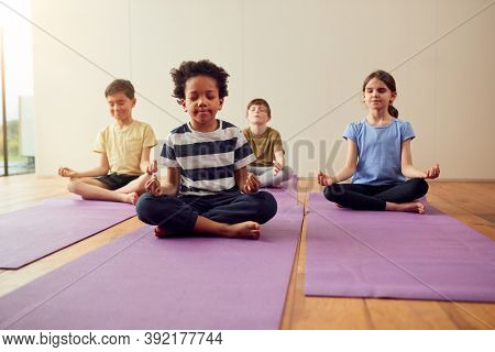Group Of Children Sitting On Exercise Mats And Meditating In Yoga Studio