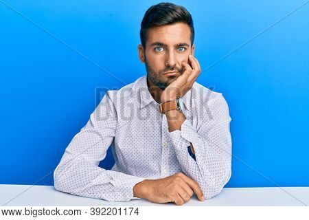 Handsome hispanic man wearing business clothes sitting on the table thinking looking tired and bored with depression problems with crossed arms. 