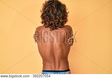 Young hispanic man standing shirtless hugging oneself happy and positive from backwards. self love and self care 