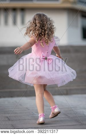 Little Girl In Pink Dress Spinning Around On The Street. Back View