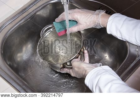 Woman's Hands With Gloves Washing Dish With Fresh Water At Kitchen Faucet Over The Metal Sink. Human