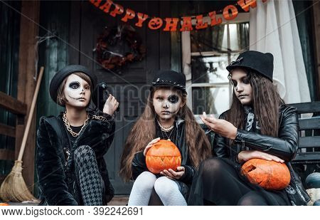 Scary Girls, Sisters, Friends Celebrating Halloween.treak Or Treat Game.pumpkins.sitting On Porch St