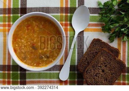 Top View Of Soup Of Kharcho, Spoon, Bread And Green On The Tablecloth With Lines