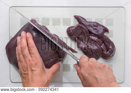 Top View Of Woman Hands Cutting Raw Piece Of Liver On Glass Cutboard On Slices Using Knife On White 