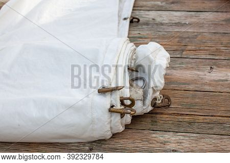 A White Jib Sail Rolled Up On The Dock With Shows A Close Up Of The Bolt Rope And Copper Hanks Sewn 