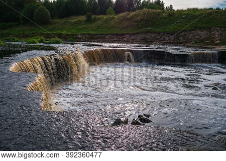 Waterfall, Water Flowing From The River Falls Down. A Stormy River With A Brown Hue.