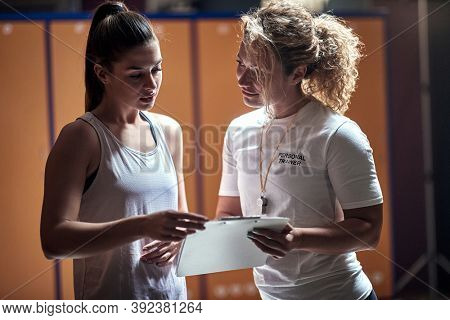 A young handsome girl and female personal trainer at the locker room discussing results. Recreation, fitness and sport