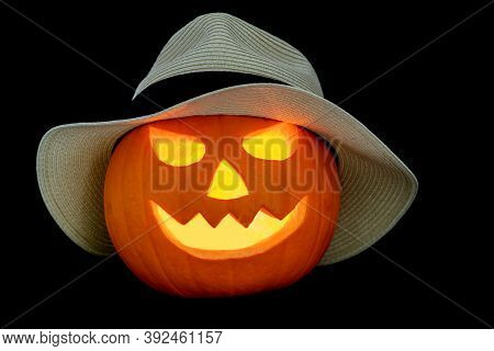 Carved Halloween Pumpkin Wearing A Straw Hat Isolated On A Black Background