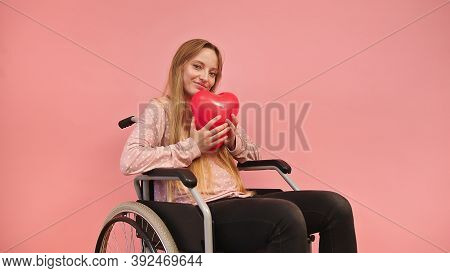 Young Caucaian Disabled Woman In Wheelchair Holding Heart Balloon. High Quality Photo