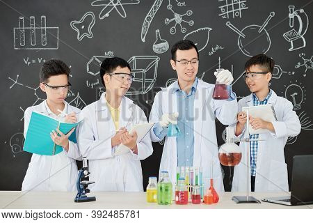 Smiling Young Asian Chemistry Teacher Showing What Liquids He Is Going To Mix To Show Chemical React