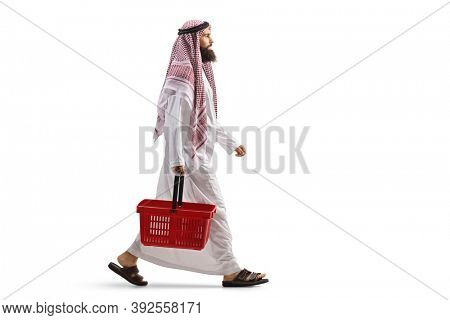 Full length profile shot of an arab man in a thobe walking with a shopping basket isolated on white background