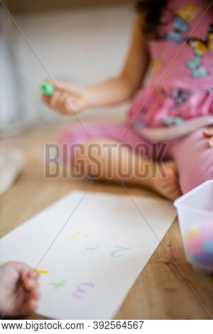 Little Girl Doing Sums On A Paper Sheet With A Textmarker On The Wooden Floor