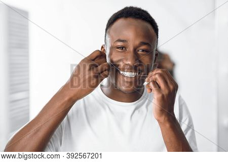 Toothcare And Hygiene. African American Guy Flossing Teeth Using Floss Smiling To Camera Standing In