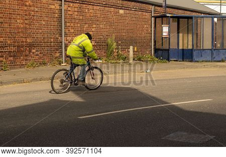 Doncaster, Yorkshire, England -  October 7, 2020. Worker Riding A Bicycle With An Hi Vis Jacket  On 