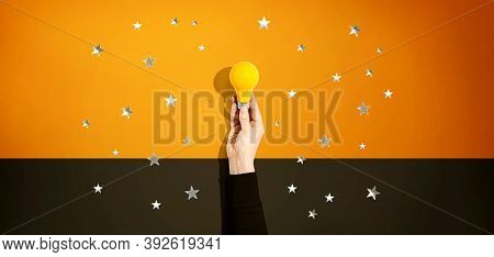 Person Holding A Yellow Light Bulb With Silver Shiny Stars