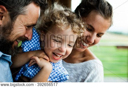 Close-up Portrait Of Family With Small Daughter By Wooden Cabin, Holiday In Nature Concept.