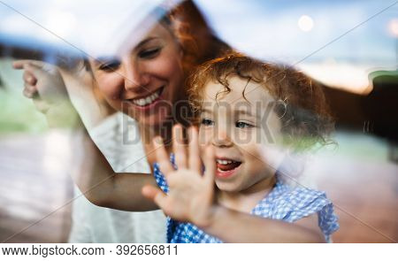 Small Girl With Mother By Window, Holiday In Nature Concept. Shot Through Glass.