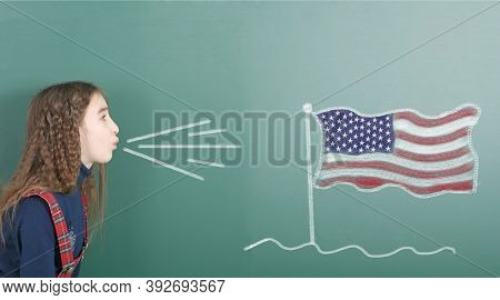 Pre-adolescent Girl Blowing On The School Board Drawn On The Blackboard American Flag. High Resoluti