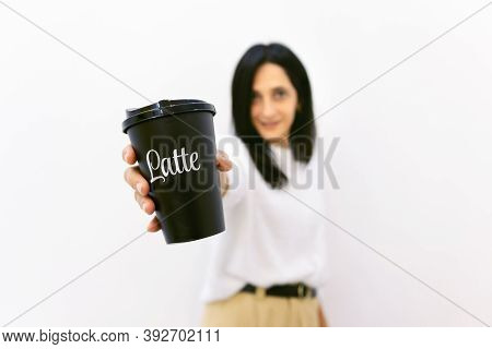 Close Up Of Disposable Black Coffee Cup With Latte Title On It Holded By Young Woman In The Backgrou