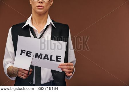 Midsection of young manlike woman in elegant suit cutting syllable fe from word female on paper so that it became male while standing in isolation