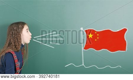 Pre-adolescent Girl Blowing On The School Board Drawn On The Blackboard China Flag. High Resolution 