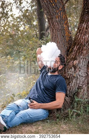 Handsome Vaper Enjoying An Electronic Cigarette Outside. Stylish Man.
