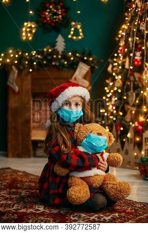 Portrait Of Cutel Little Child Girl In Medical Mask Playing With Taddy Bear, New Year Holiday Concep