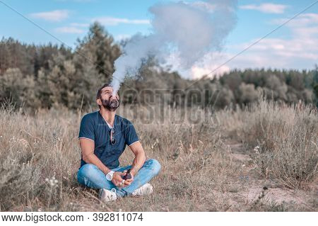 Bearded Man Blows Up A Couple An Electronic Smoke Device On The Grass. Vaping.