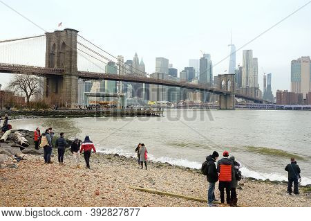 New York, Usa - December 26, 2019: Tourists Walking On Riverside Of East River And Admiring Of Famou