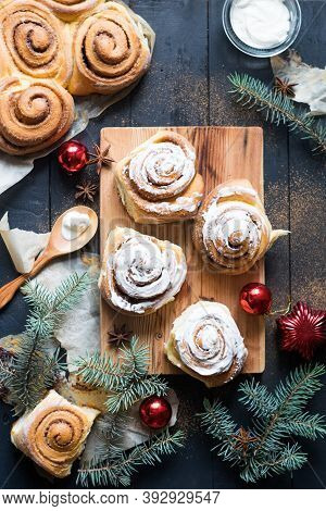 Freshly Baked Cinnamon Buns Cinnabons With Cream On Parchment Paper On Black Wooden Table With Fir-t