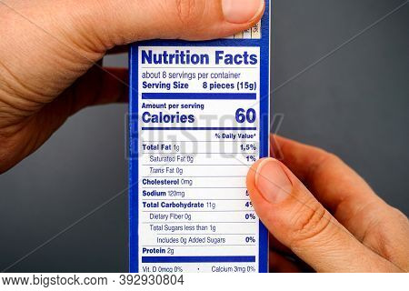 Nutrition Facts On Food Box In Woman Hands. Gray Background.