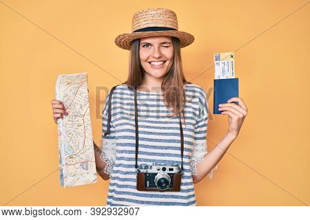Beautiful caucasian tourist woman holding city map and passport winking looking at the camera with sexy expression, cheerful and happy face. 