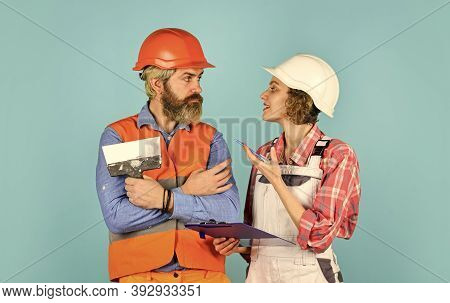 Two Parters. Couple Looking At A Blueprint. Woman And Man Wear Safety Hardhat. Family Standing Insid