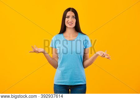 Who Knows. Portrait Of Confused Woman Shrugging Shoulders, Spreading Hands, Looking At Camera Posing