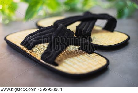 Pair Of Traditional Japanese Bamboo Zori Shoes With Decorative Greenery In The Background