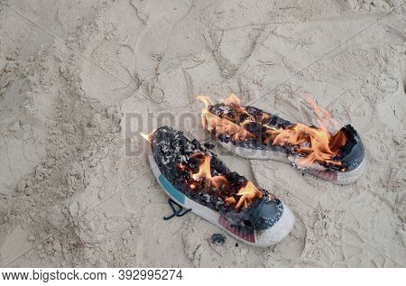Burning Sports Sneakers Or Gym Shoes On Fire Stand On Sandy Beach Coast. Athlete Burned Out. Physica