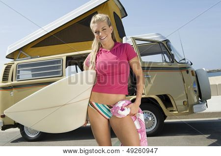 Portrét smějící se mladé ženy držící Surf proti campervan