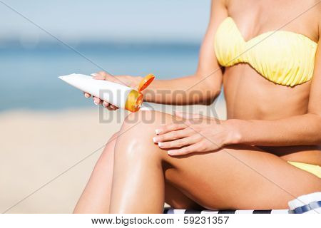 summer holidays and vacation - girl putting sun protection cream on the beach chair