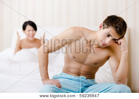Married couple quarrels in bed. Depressed man sitting on the edge of the bed, focus on man
