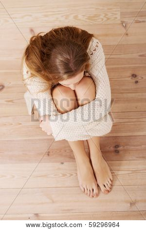 Beautiful caucasian woman is sitting on the floor. Looks as she were hiding from sth.