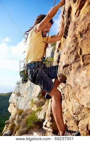 A dreadlock rock climbing guy finding a foothold on a steep mountain