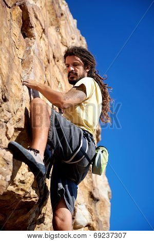 A rock climber finding a foothold on the steep mountain he's climbing