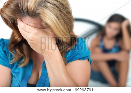 Sad and worried mother with her troubled teenage daughter in the background