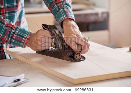 Cropped image of carpenter's hand using plane on wood at workshop