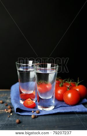 Glasses of ouzo and tomatoes on wooden table, on grey background