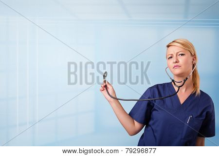 Pretty young nurse in hospital listening to empty copy space with sthetoscope