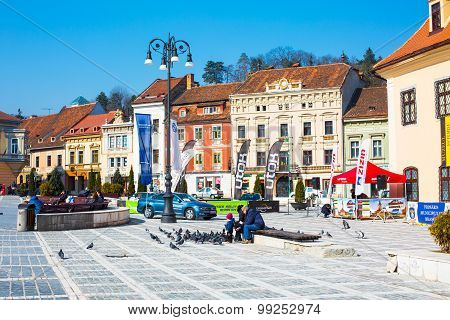People Feeding The Pigeons At Council Square In Downtown Of Brasov, Romania.