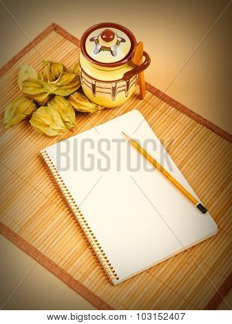 Physalis Fruits, Ceramic Sugar Bowl And A Notebook On A Bamboo N