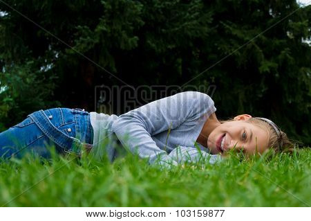 Young Cute Child Girl Lays On Stomach In Summer Grass Smiling
