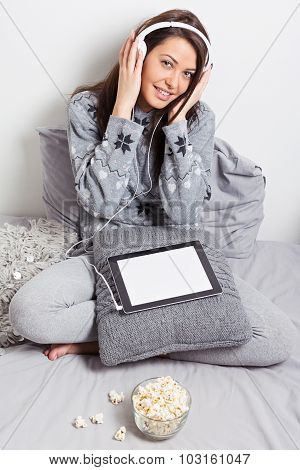 Teenage girl with headphones and tablet sitting in bed